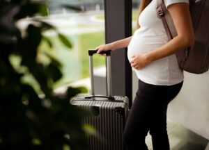 Reisen in der Schwangerschaft: Schwangere Frau mit Rollkoffer und Rucksack auf
